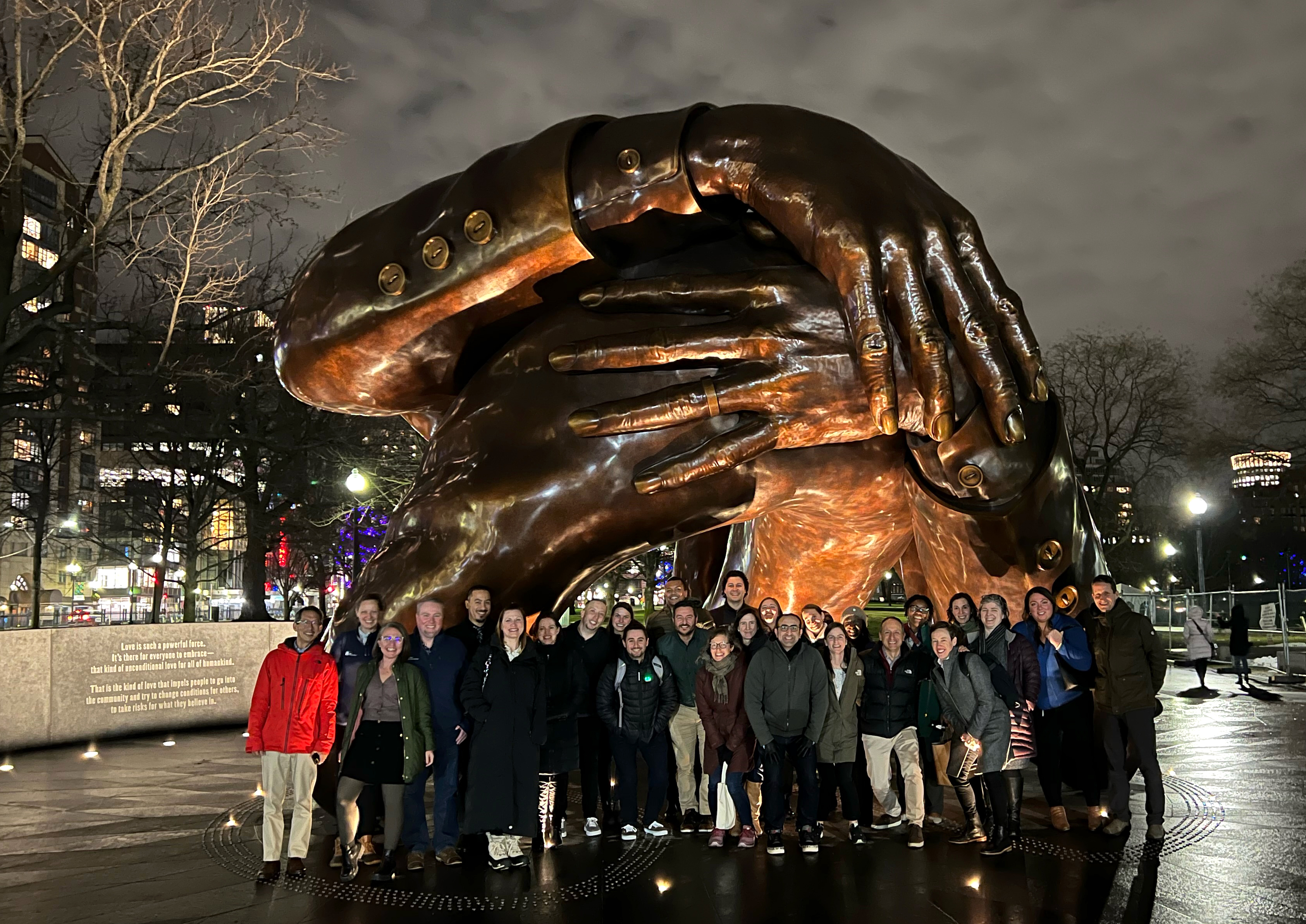 Barr staff members gather in front of the Embrace artwork at night