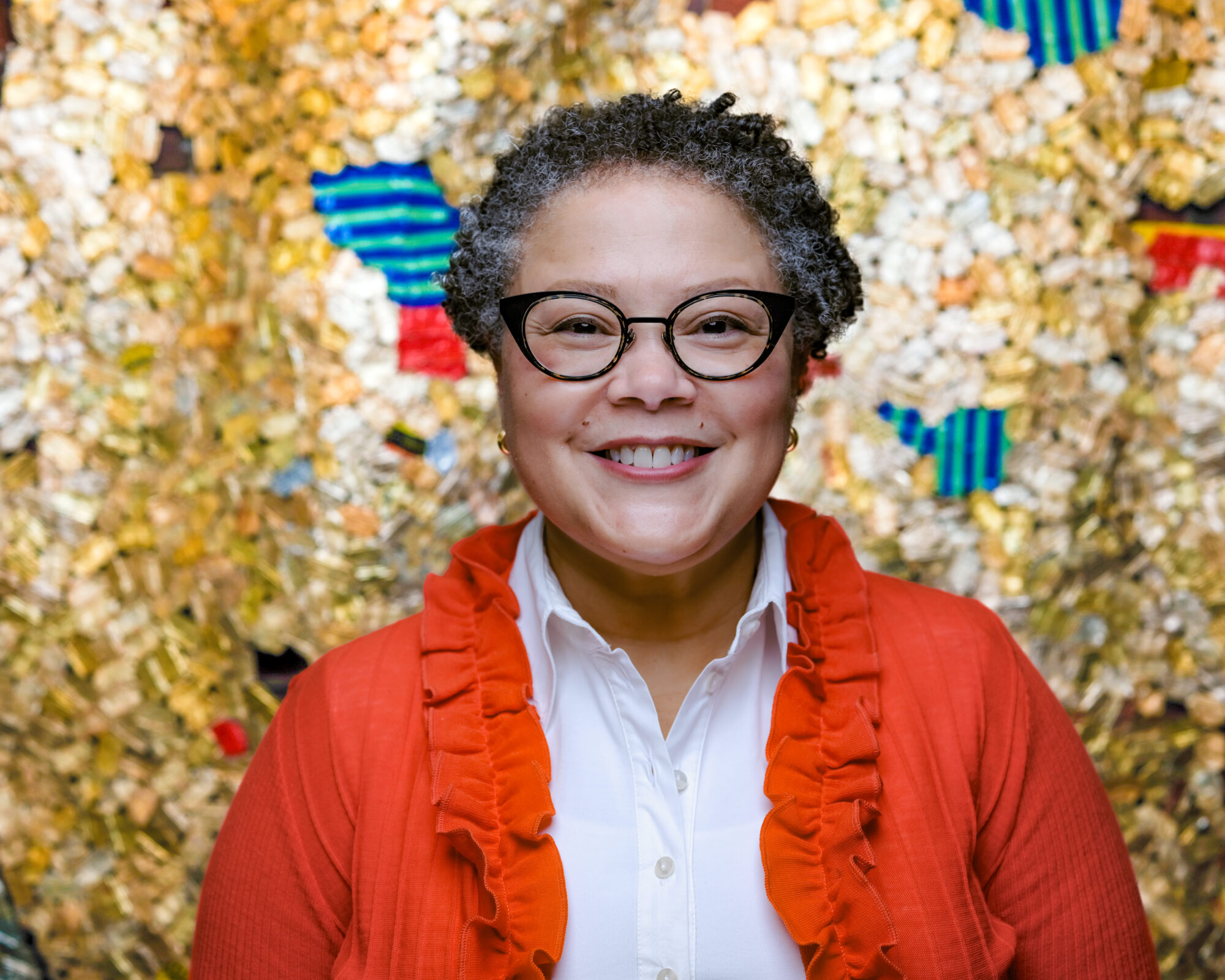 Kim Haskins wears glasses and a red ruffled sweater. She smiles warmly.