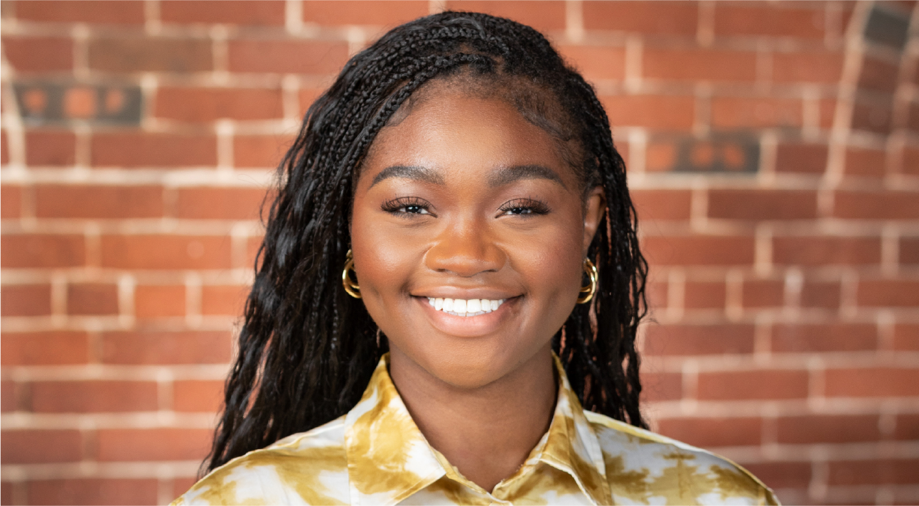 Cassie Bruny poses for a headshot. She has long braids and smiles brightly.