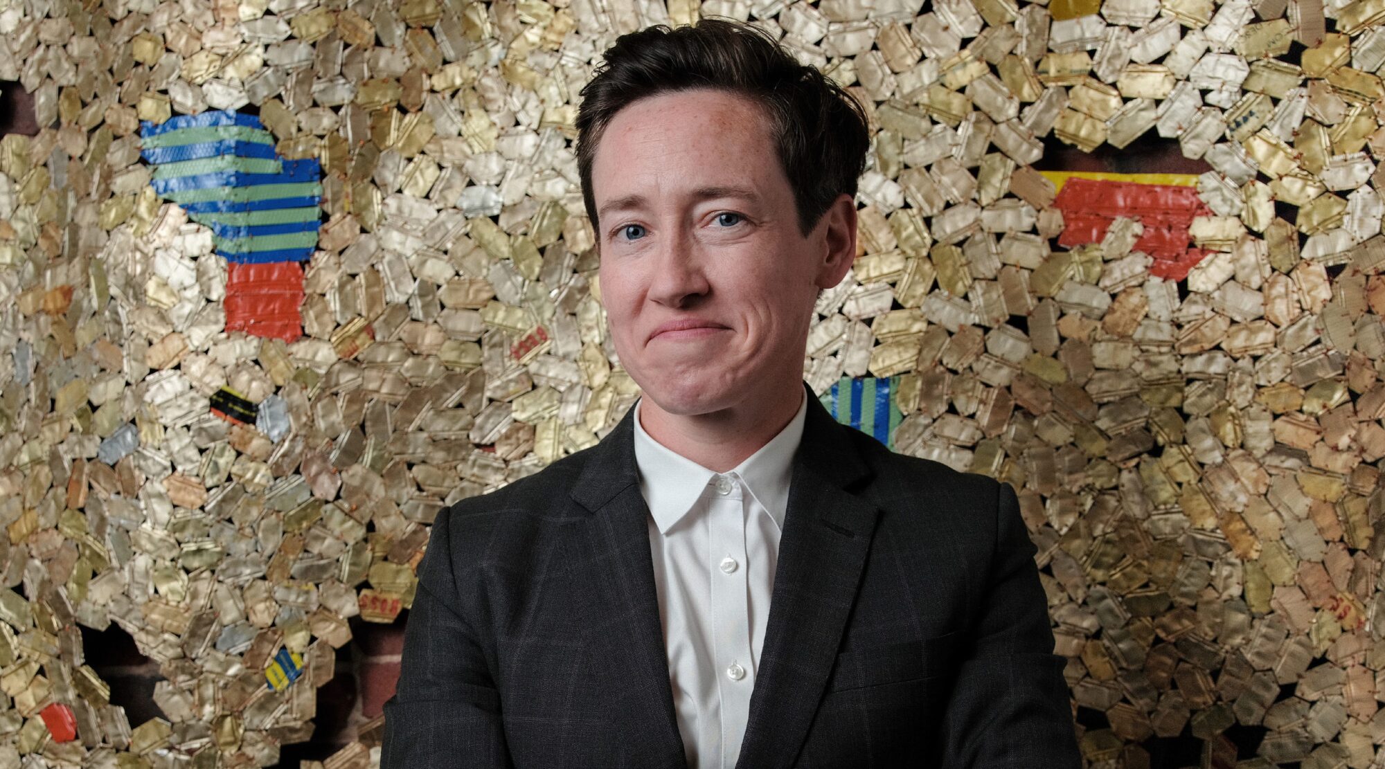 Rory Neuner poses for a headshot. She wears a crisp suit and smiles playfully.