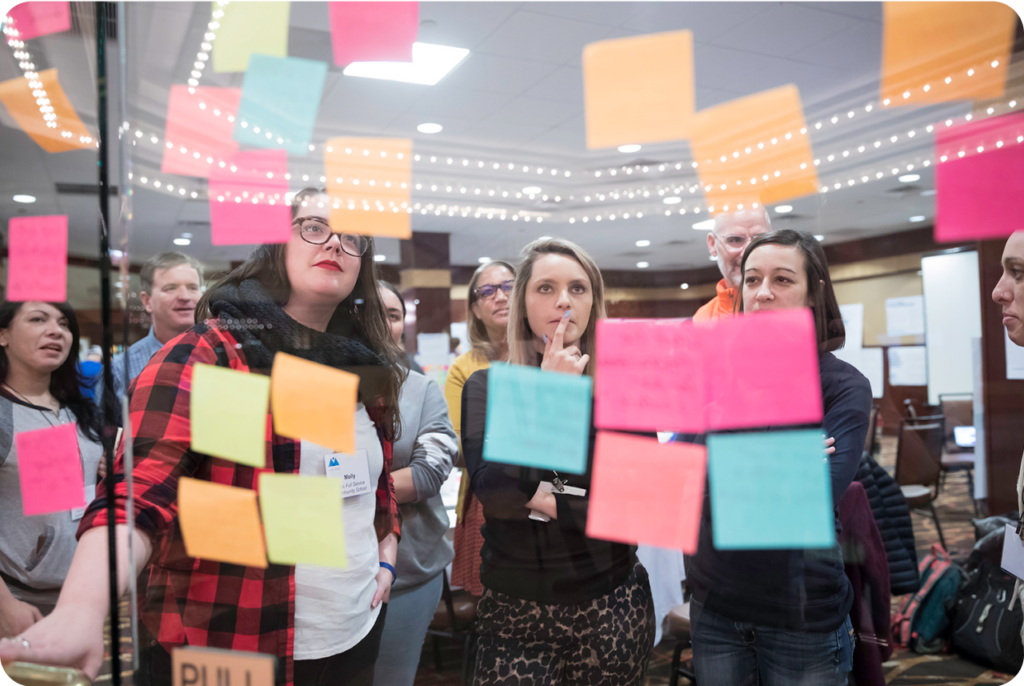 People putting sticky notes on a clear wall.