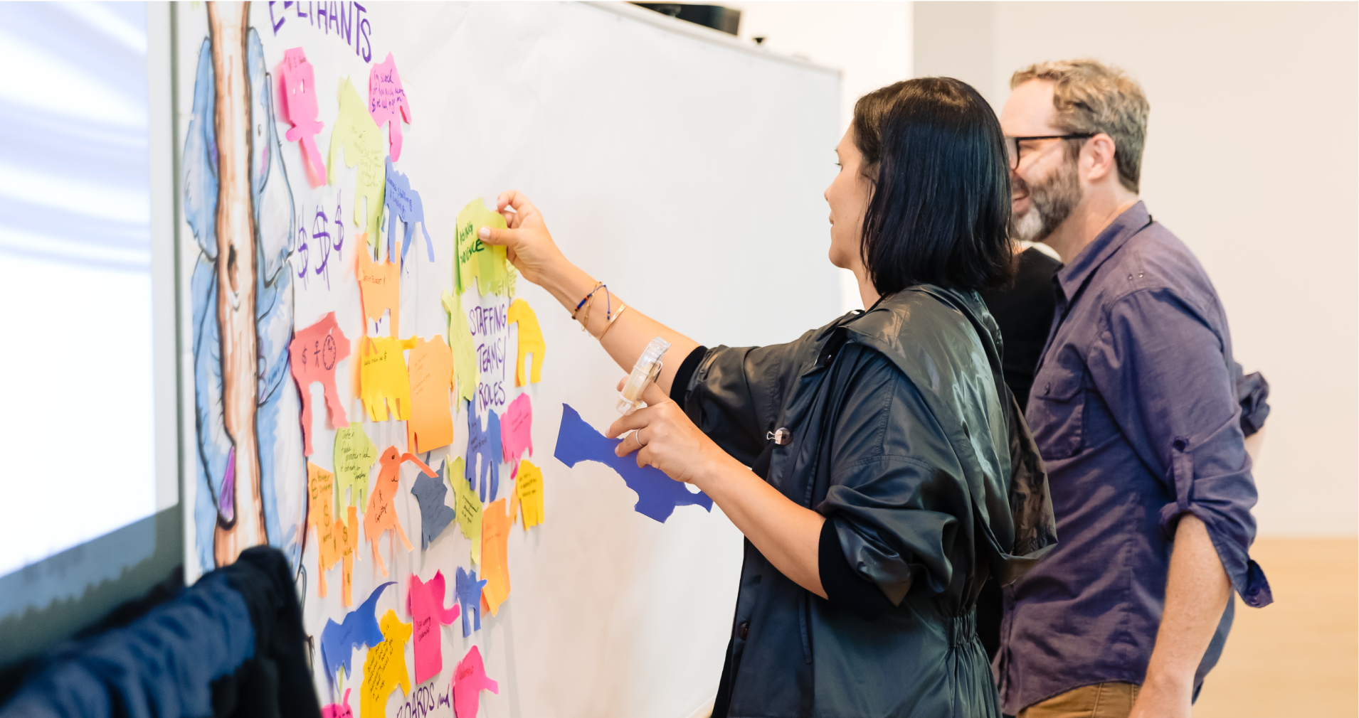 People taping paper cutouts to a white board.