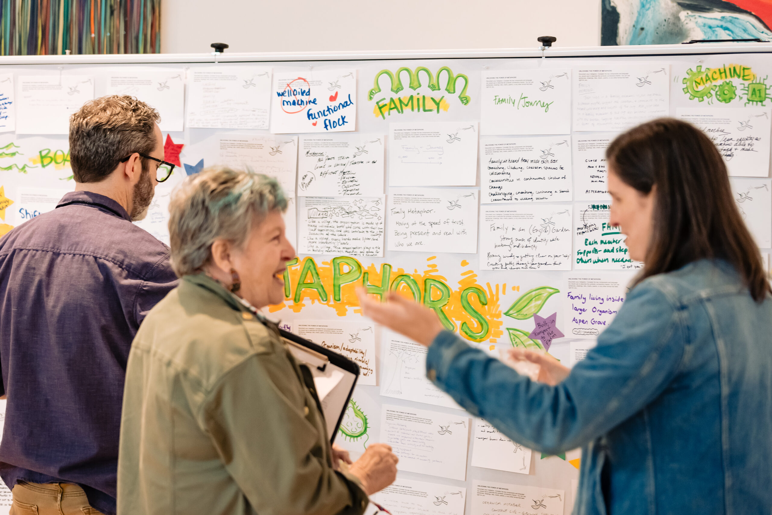 Two people talking in front of a graphic artist writing notes on a white board