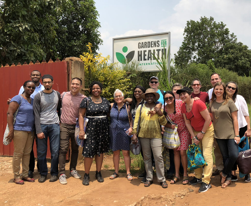 Group of Barr Fellows wear colorful clothes and pose in front of a garden sign in Rwanda.
