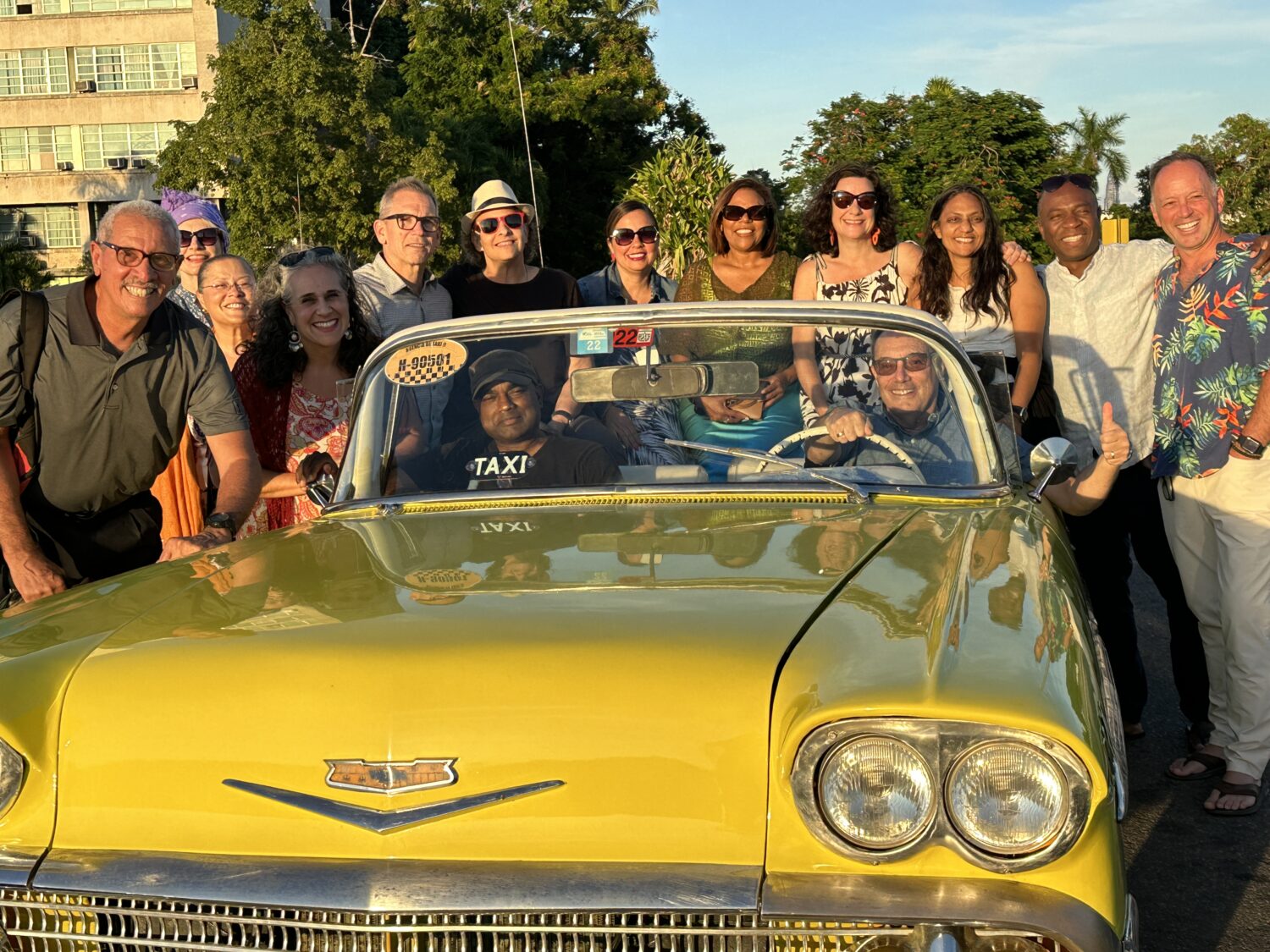 A group of people sit in and crowd around a yellow taxi in Cuba