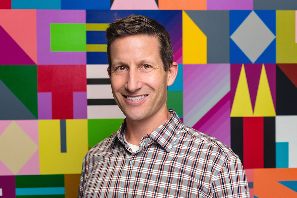 Stefan Lanfer poses for a headshot. He wears a checkered shirt and smiles.