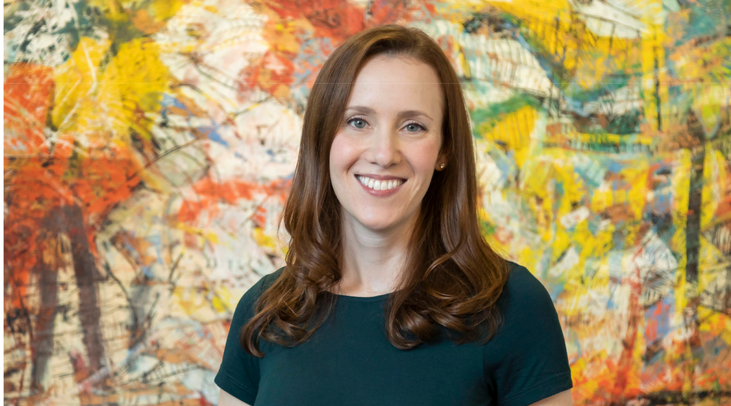 Ali Gross poses for a headshot. She has red hair, wears a dark green top, and smiles warmly.