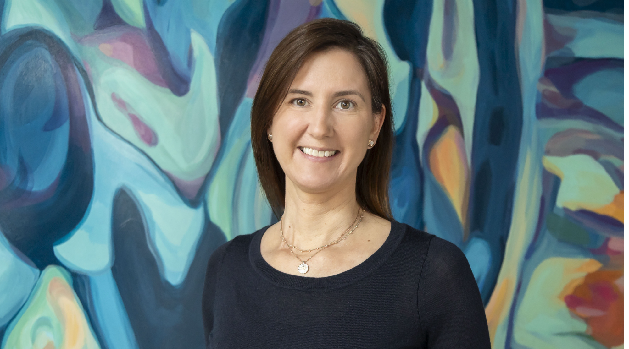 Anya Rooney poses for a headshot. She wears a scoop-neck sweater and smiles.