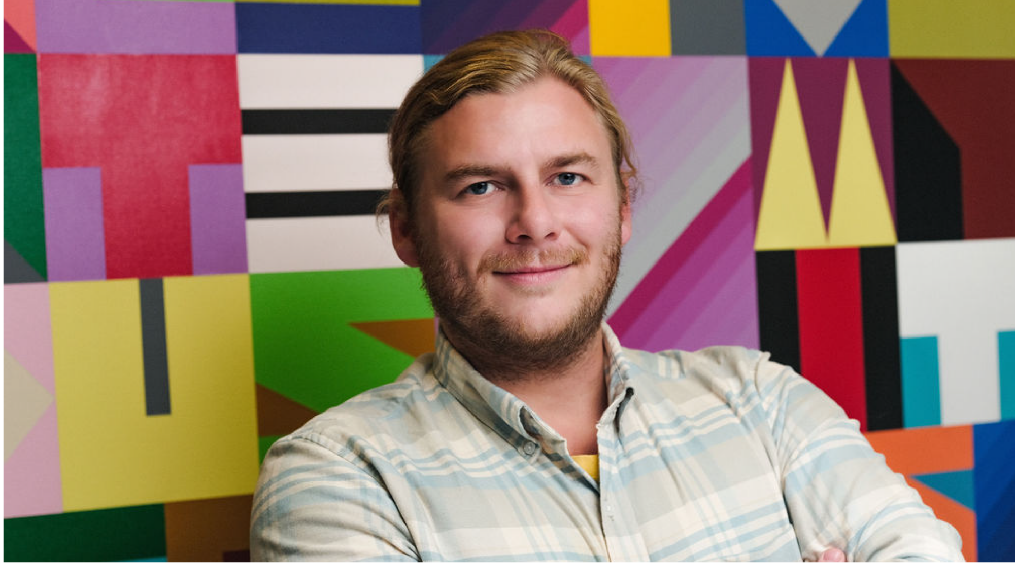 Chris Overton poses for a headshot. He has blonde hair, and wears a striped shirt. He smiles warmly.