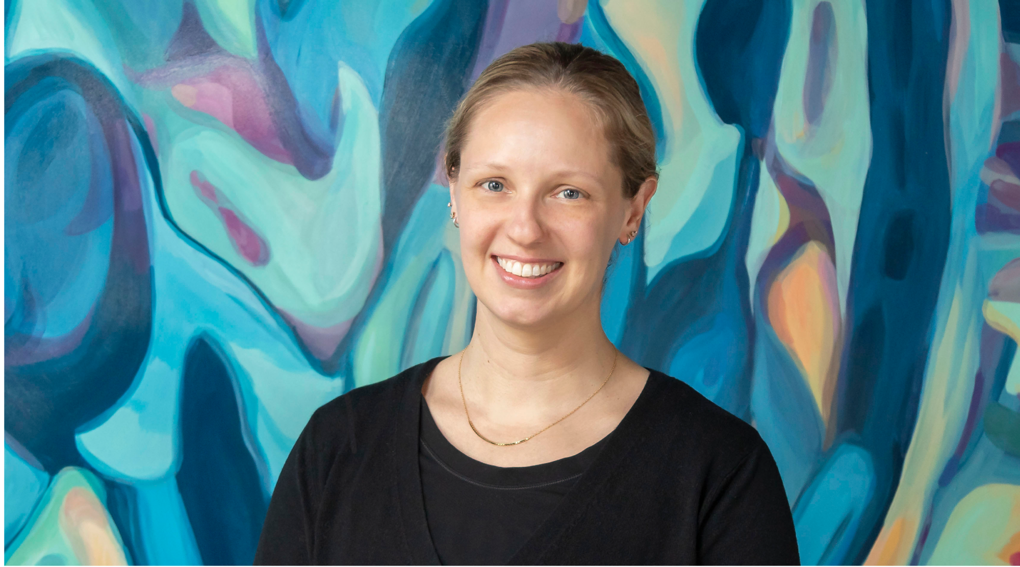 Christi Craig poses for a headshot. she wears a black top and smiles warmly.