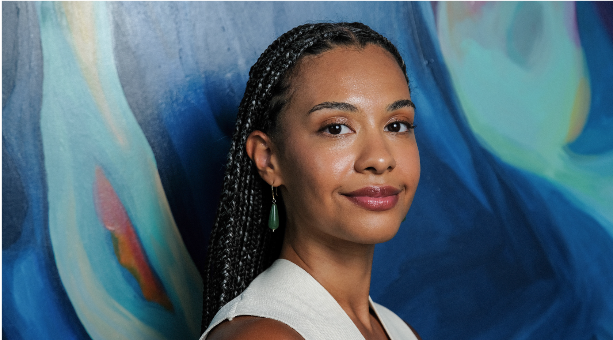 Ellie Winter poses for a headshot. She has long box braids and smiles warmly.