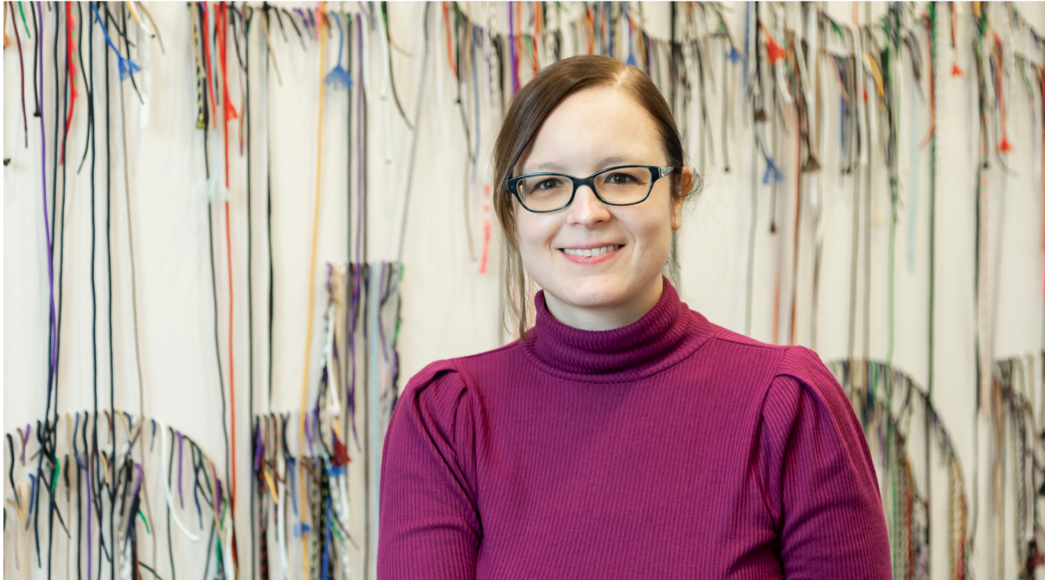 Emily Sidla poses for a headshot. She wears a magenta sweater and glasses.