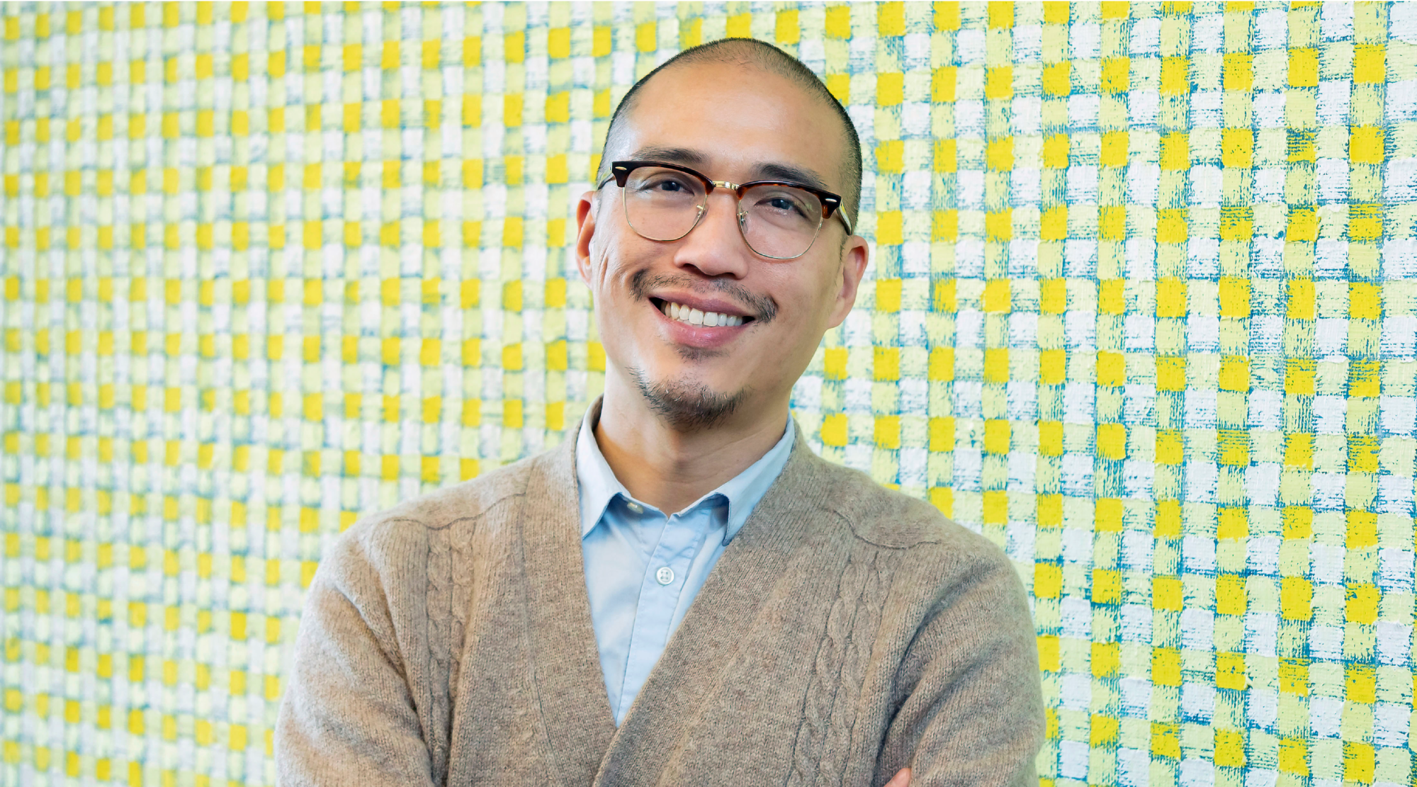 Giles Li poses for a headshot. He wears glasses and a neutral cardigan. He smiles warmly.