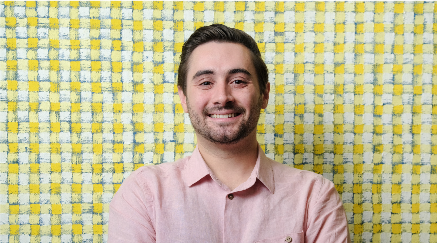 John Dello Russo poses for a headshot. He wears a pink polo shirt and smiles joyfully.