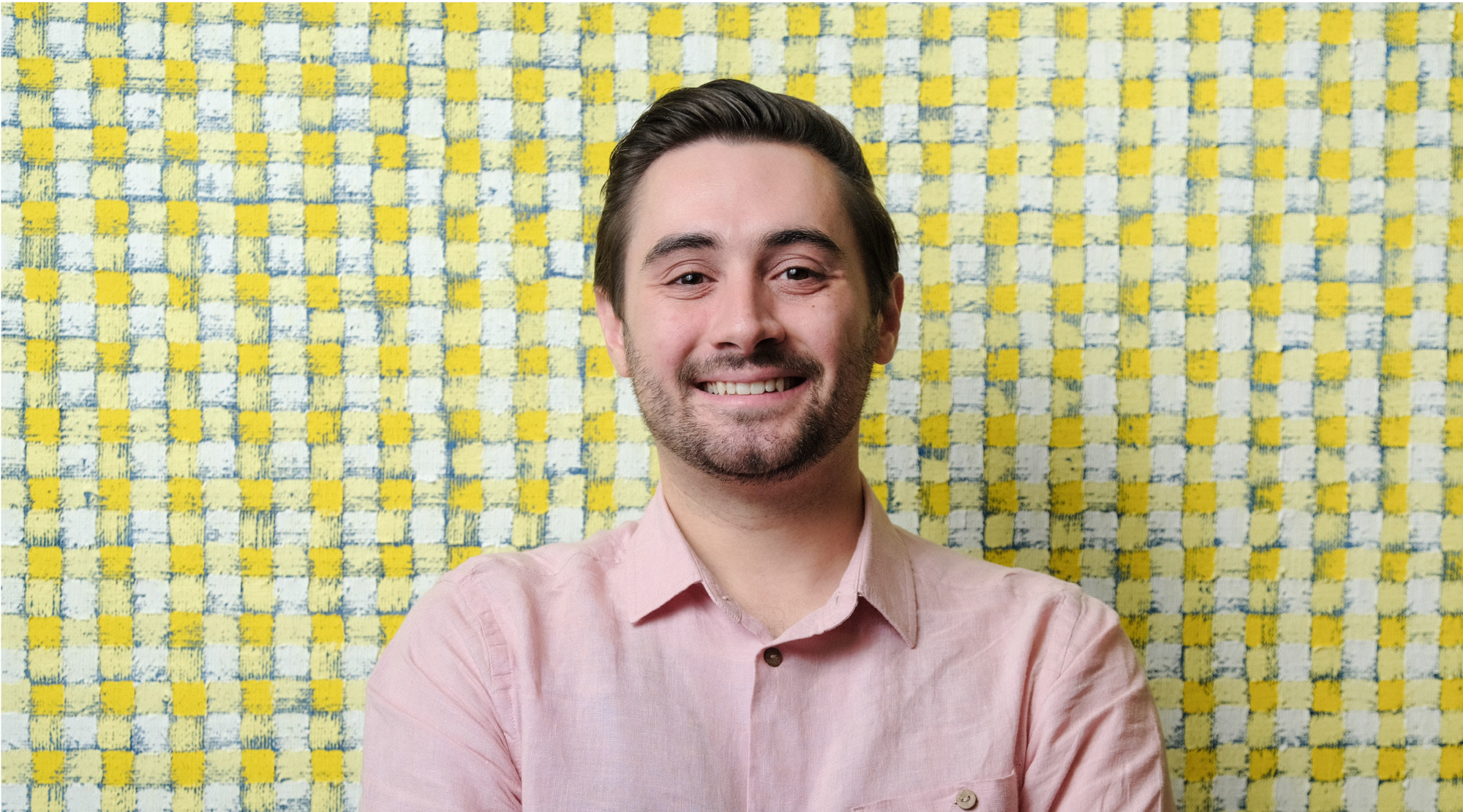 John Dello Russo poses for a headshot. He wears a pink polo shirt and smiles joyfully.