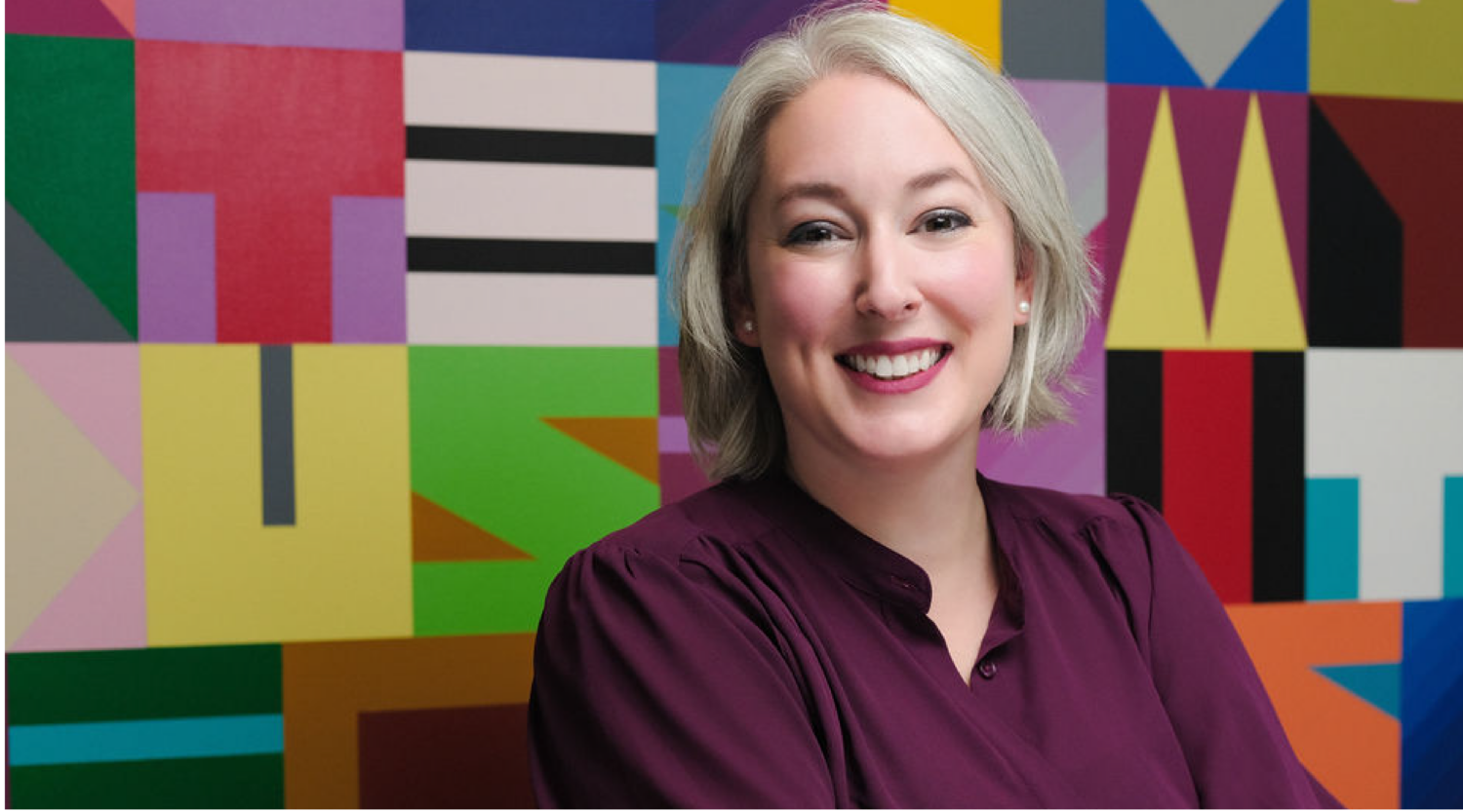 Jess Rose poses for a headshot. She has silver hair, wears bright red lipstick, and smiles warmly.