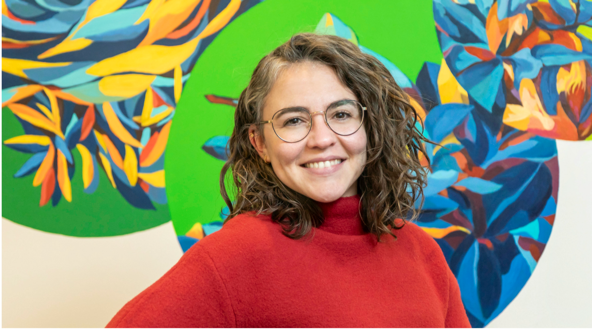 Jill Valdéz Horwood poses for a headshot. She wears glasses and a bright read sweater.