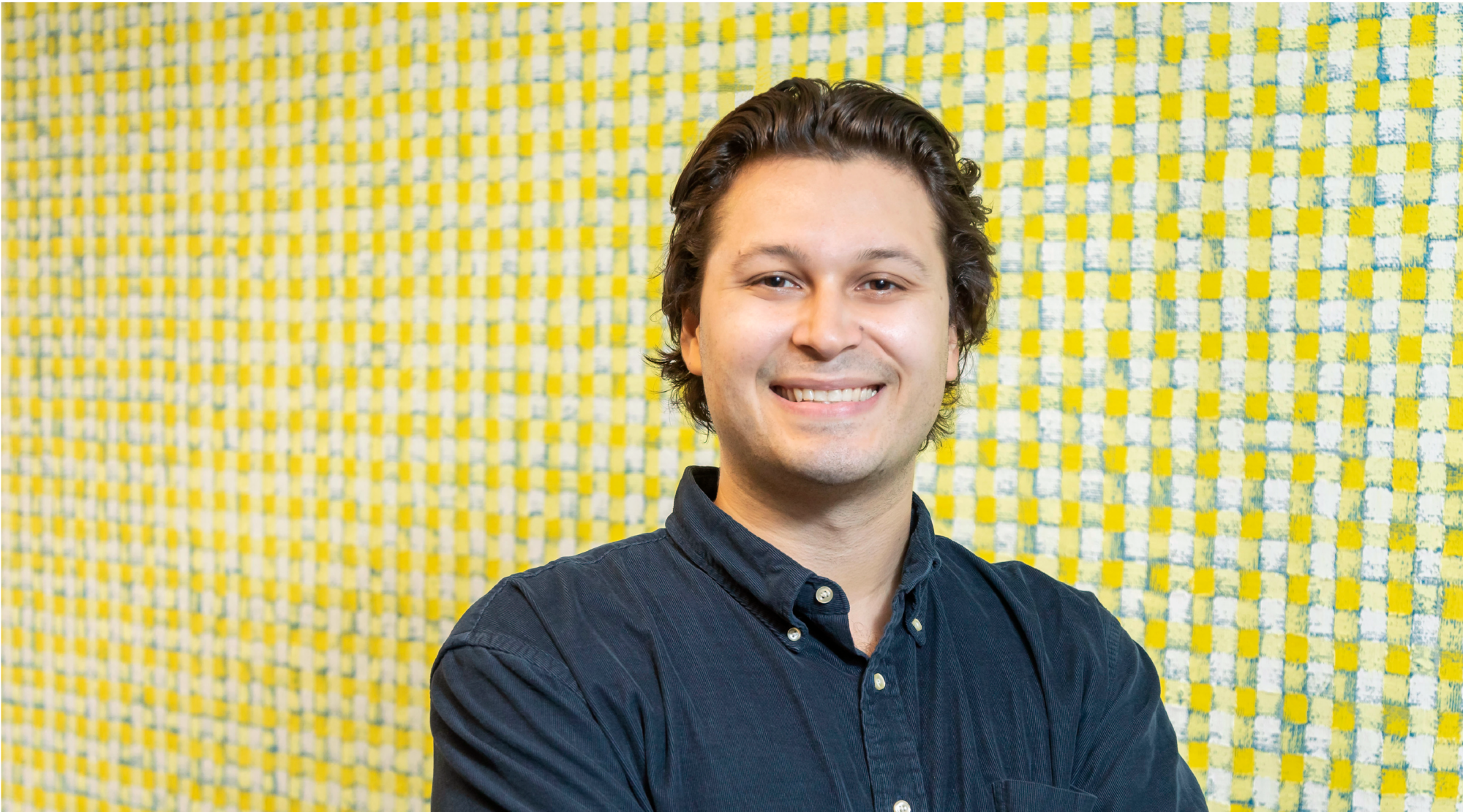 Joe Rodriguez poses for a headshot. He wears a blue button down and crosses his arms. He smiles warmly.
