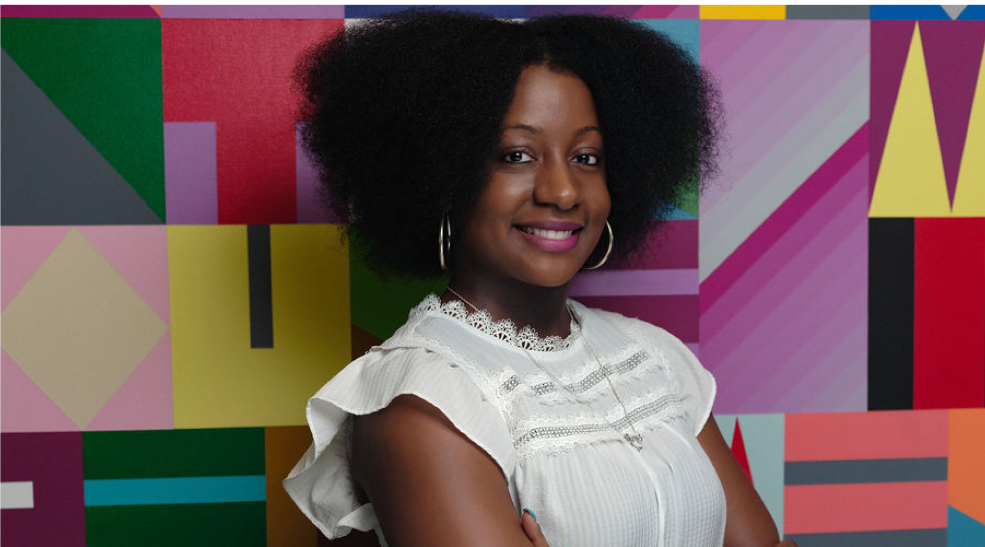 Kadeajah Goslin poses for a headshot. She wears a white top with ruffles with her natural curls down. She smiles warmly.