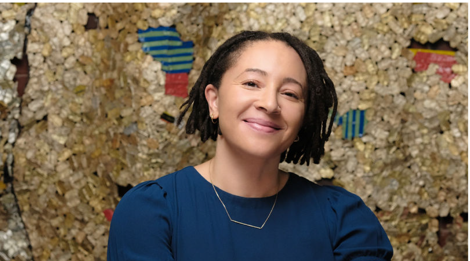 Kalila Barnett poses for a headshot. She wears a blue top and her locs are styled into a bob. She smiles warmly.