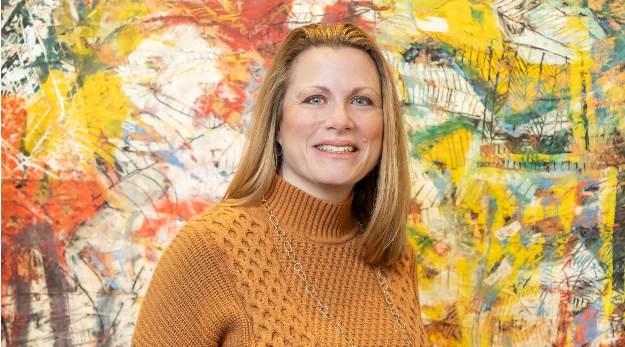 Kerri Hurley poses for a headshot. She has blonde hair and wears an orange sweater. She smiles warmly.