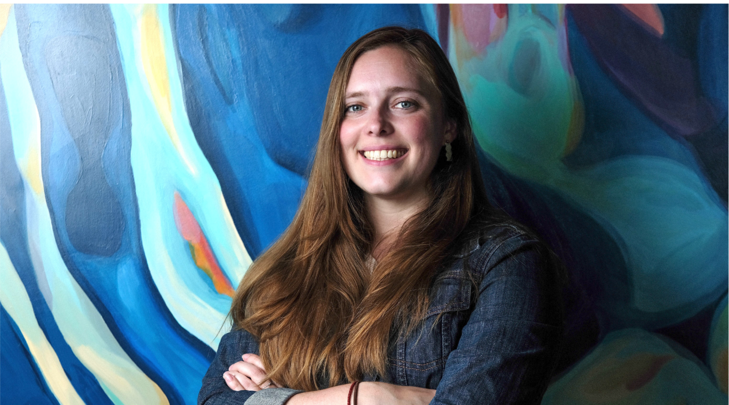 Leah Bennett poses for a headshot. She has long brown hair and wears a denim jacket. She smiles warmly.