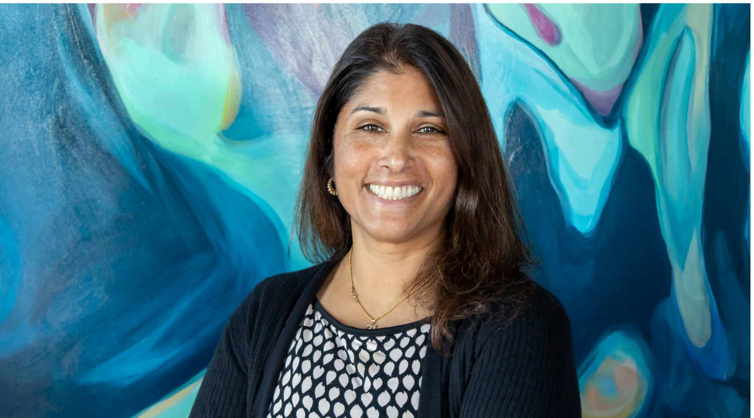 Manjula Karamcheti poses for a headshot. She wears a black sweater and has long hair. She smiles warmly.