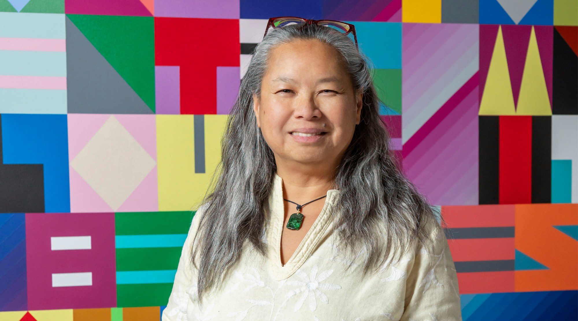 San San Wong poses for a headshot. She has long silver hair, wears a flowy white top, and smiles warmly.