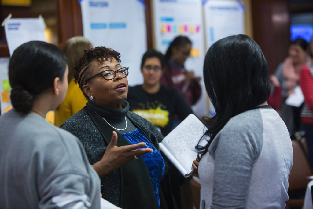 Three women engaged in conversation in a conference room with post its and active learning, conversation.