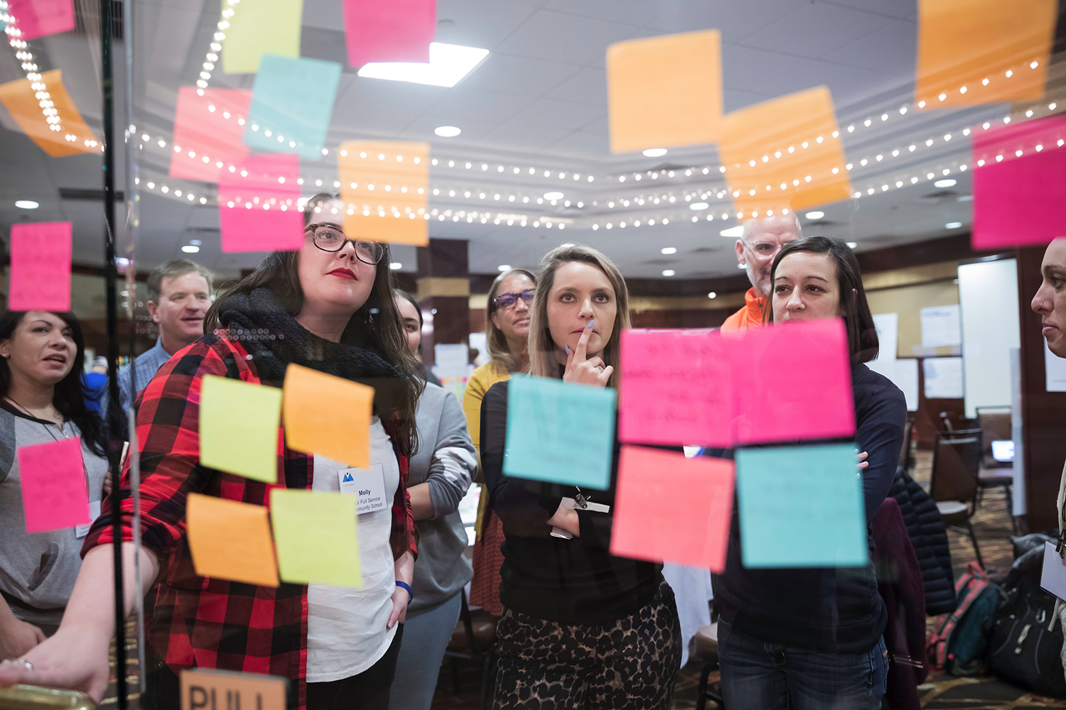A group of education professionals read colorful post its scattered on a glass wall