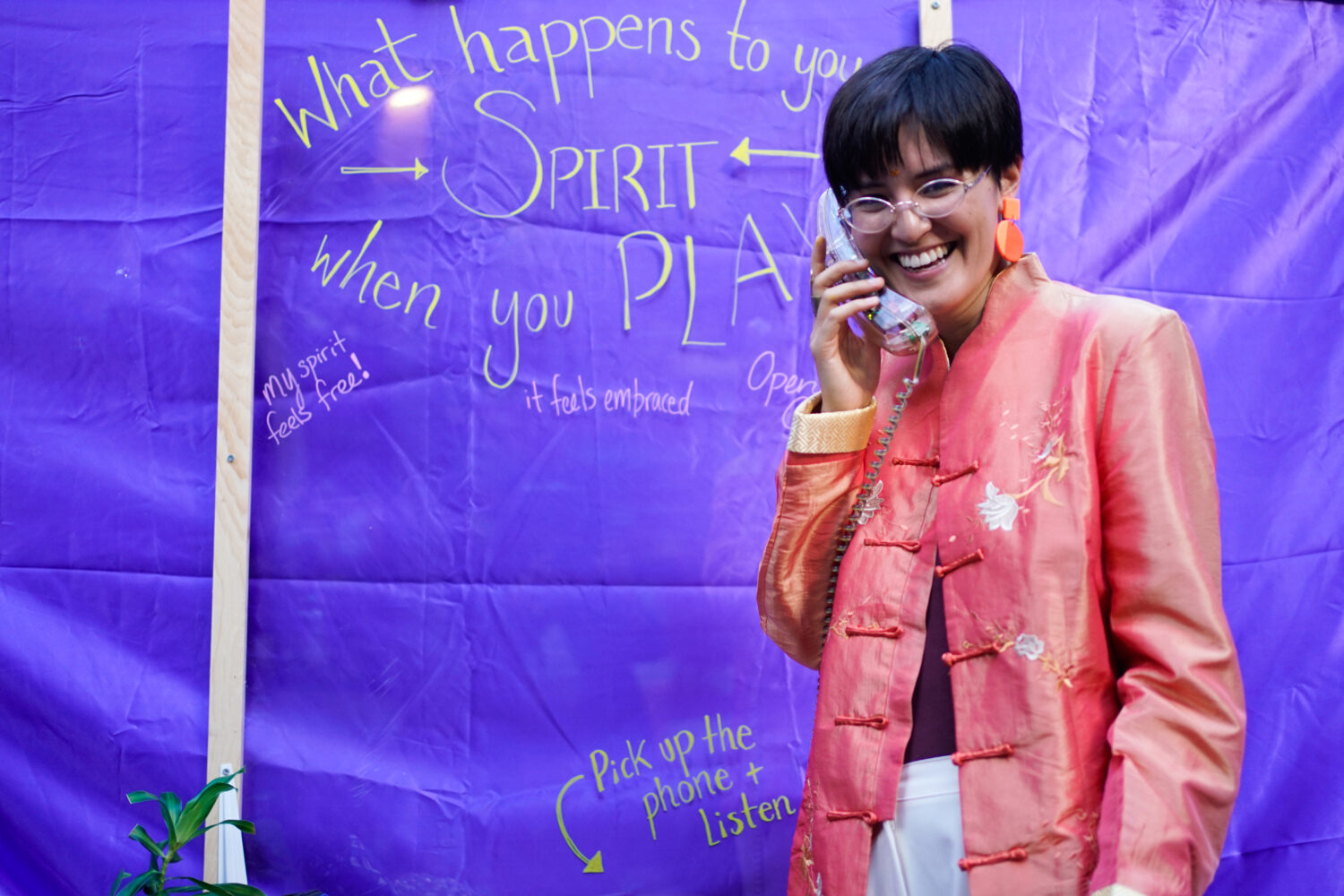A patron interacts with an art installation. Behind them, a wall reads "what happens to your spirit when you play?"