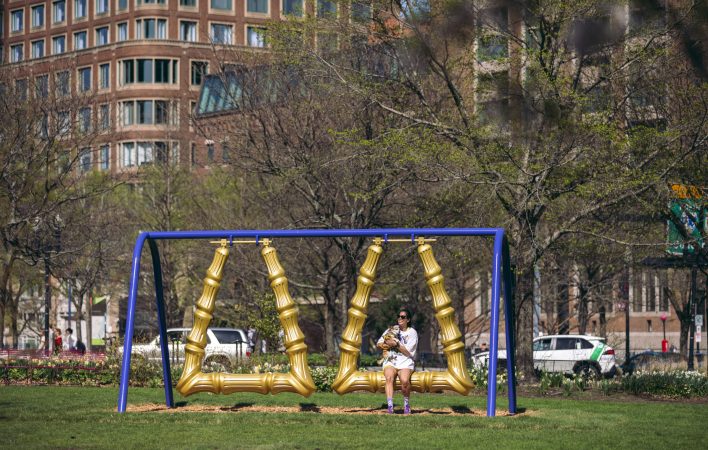 Visitors swing on a public art piece--playground swings styled like gold earrings.