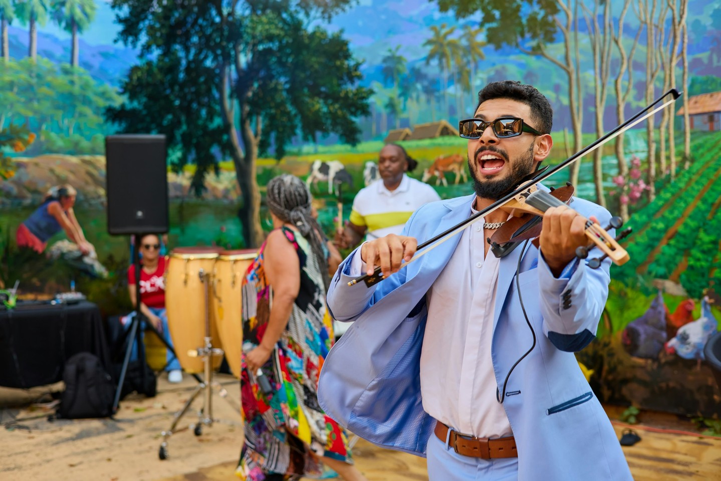 A violinist plays a public show in front of a vibrant mural.