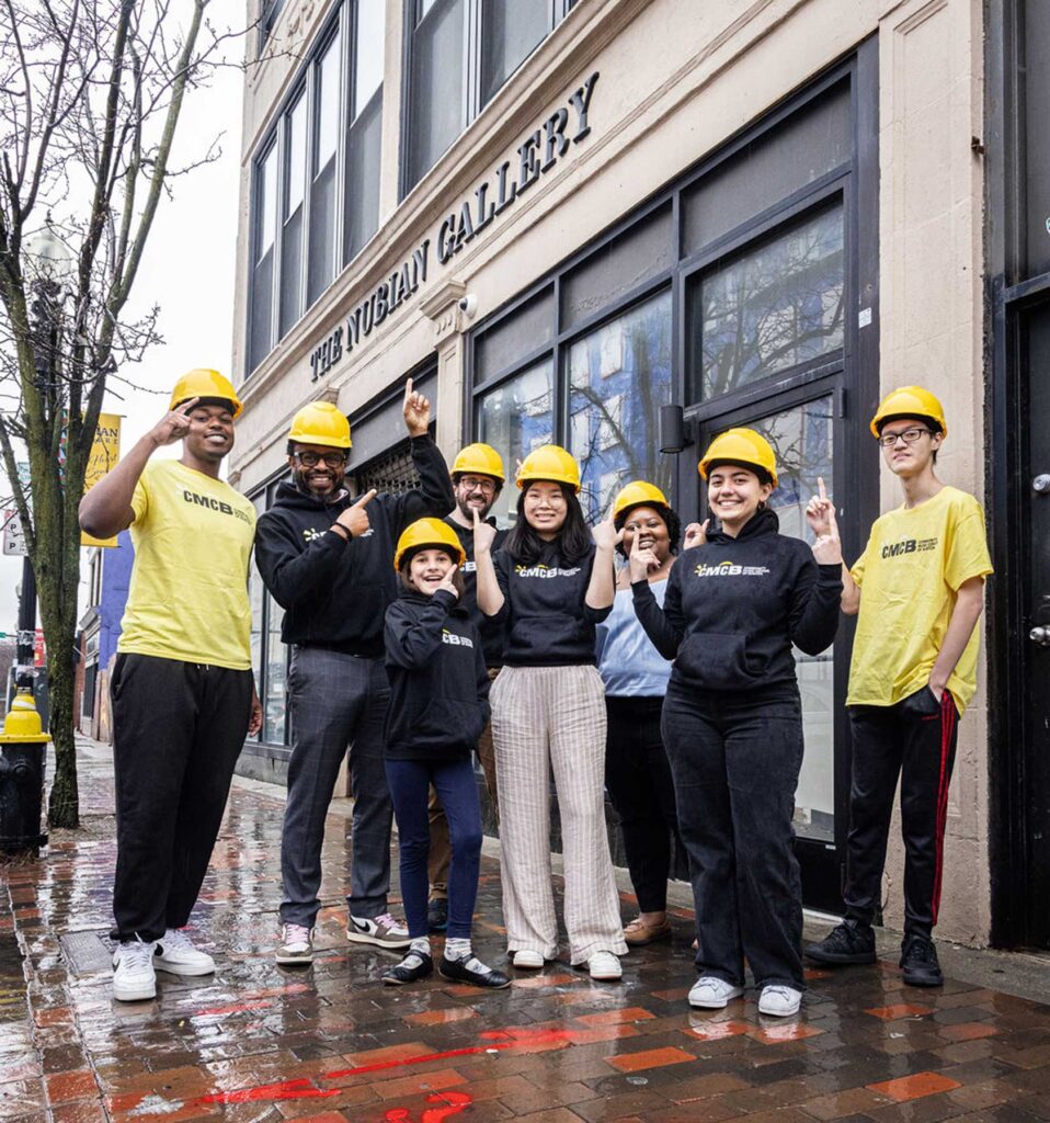 Staff members at the Community Music Center of Boston wear hard hats outside of their new art space.