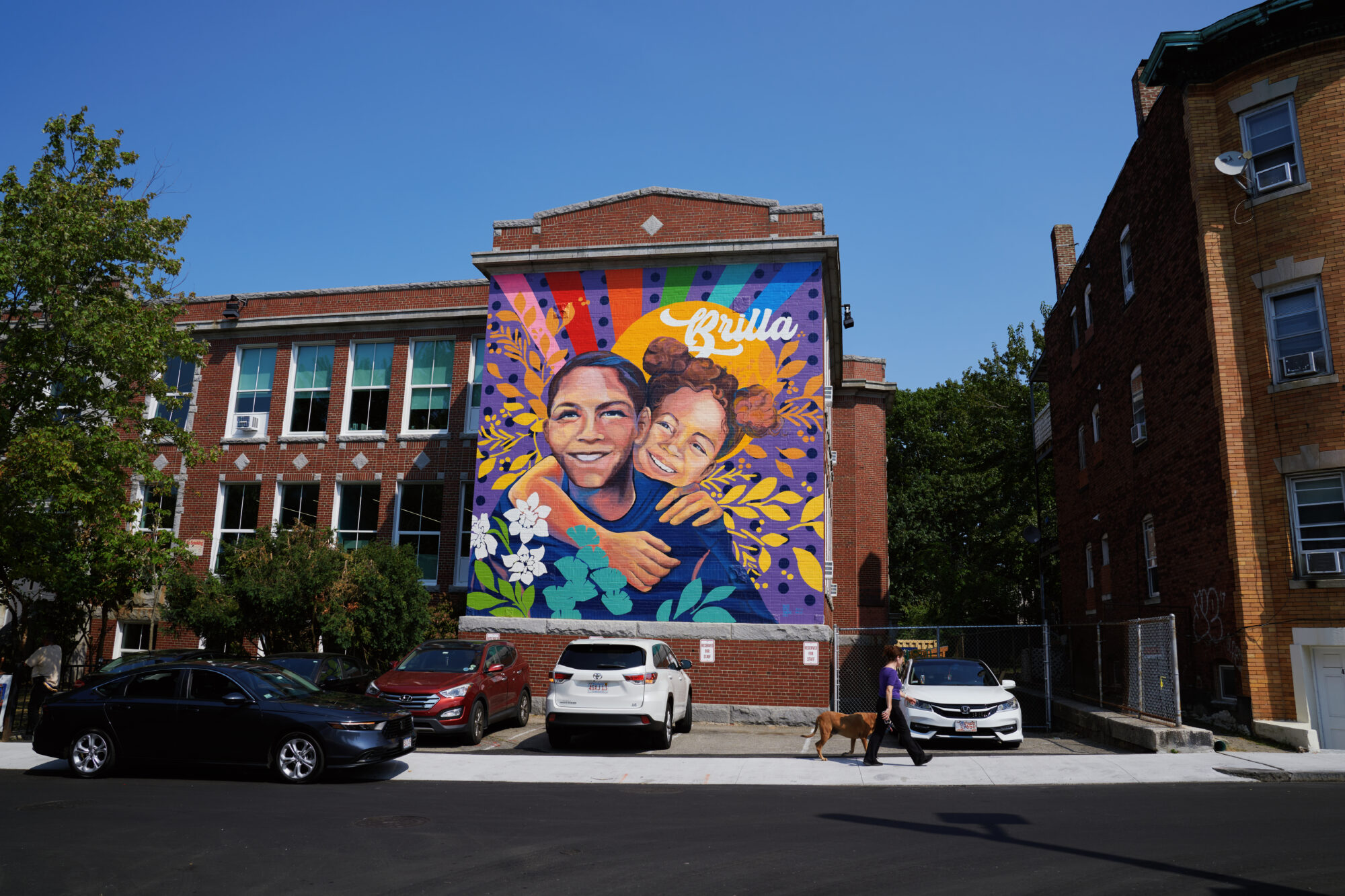 A vibrant mural on a brick building depicts two people hugging.