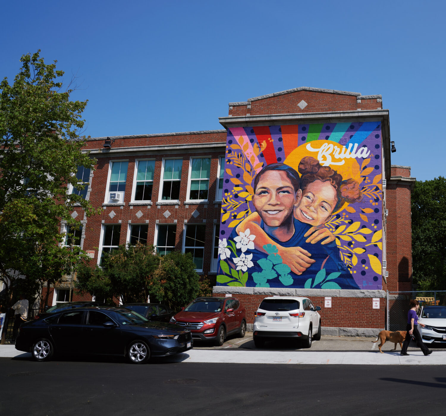 A vibrant mural on a brick building depicts two people hugging.