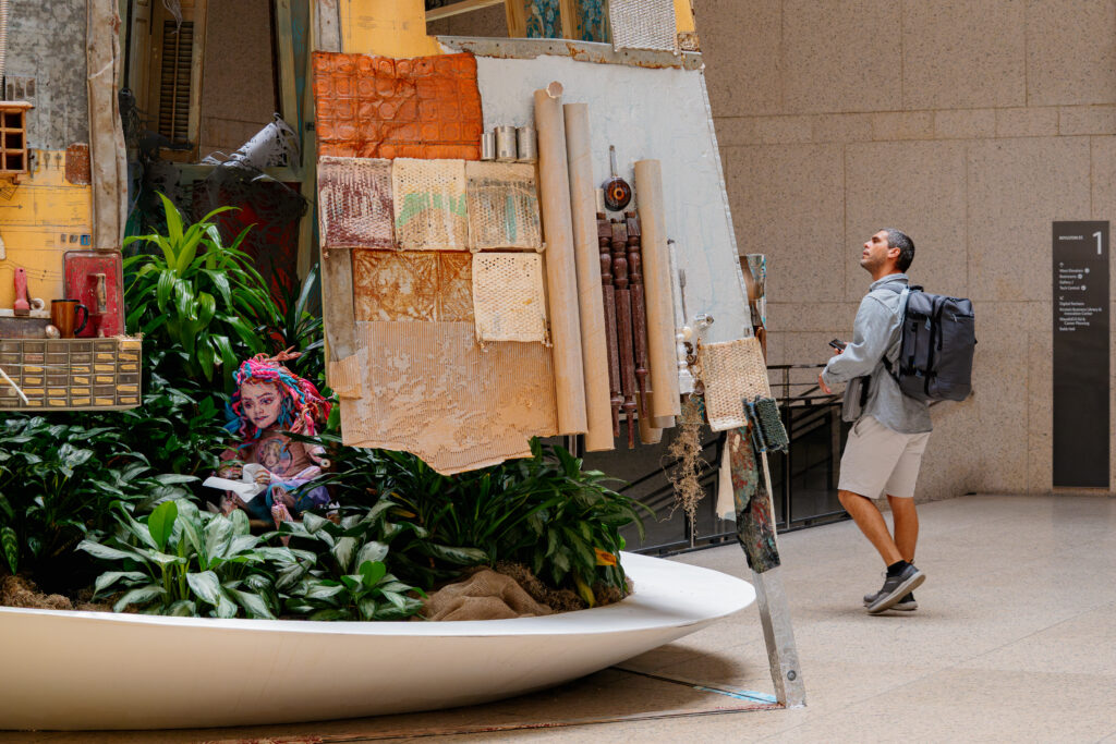 A visitor takes in a large public art installation made of plants, sculpture, and found objects.