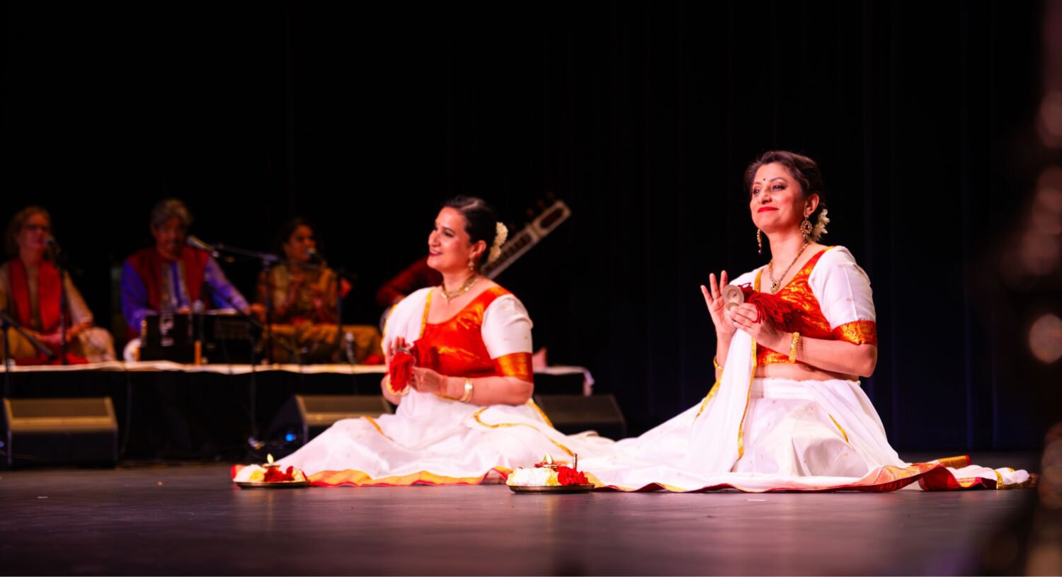 Two women performers sitting on stage