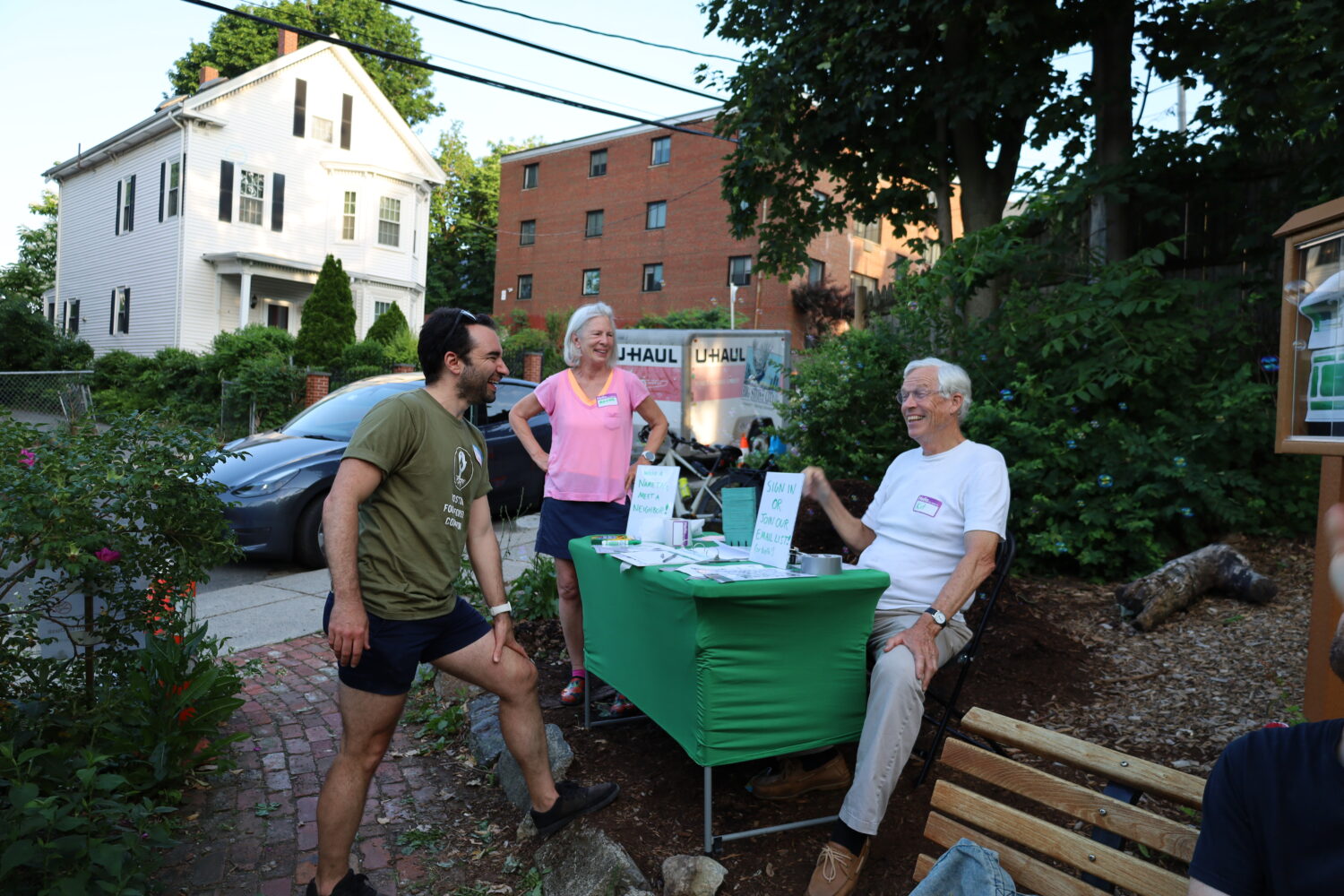 Three people are laughing around a green sign in table at a meeting at Upham's corner food forest